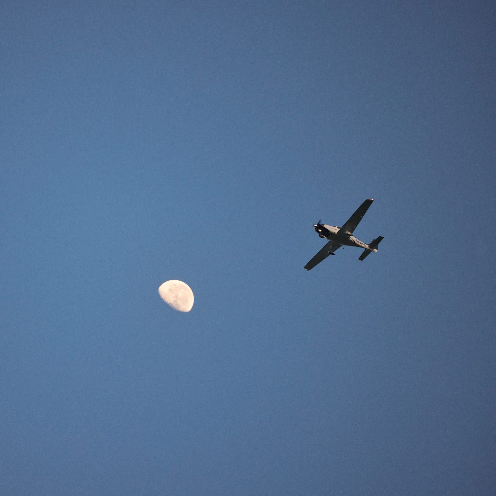 Plane flying with clear blue skies and a half moon